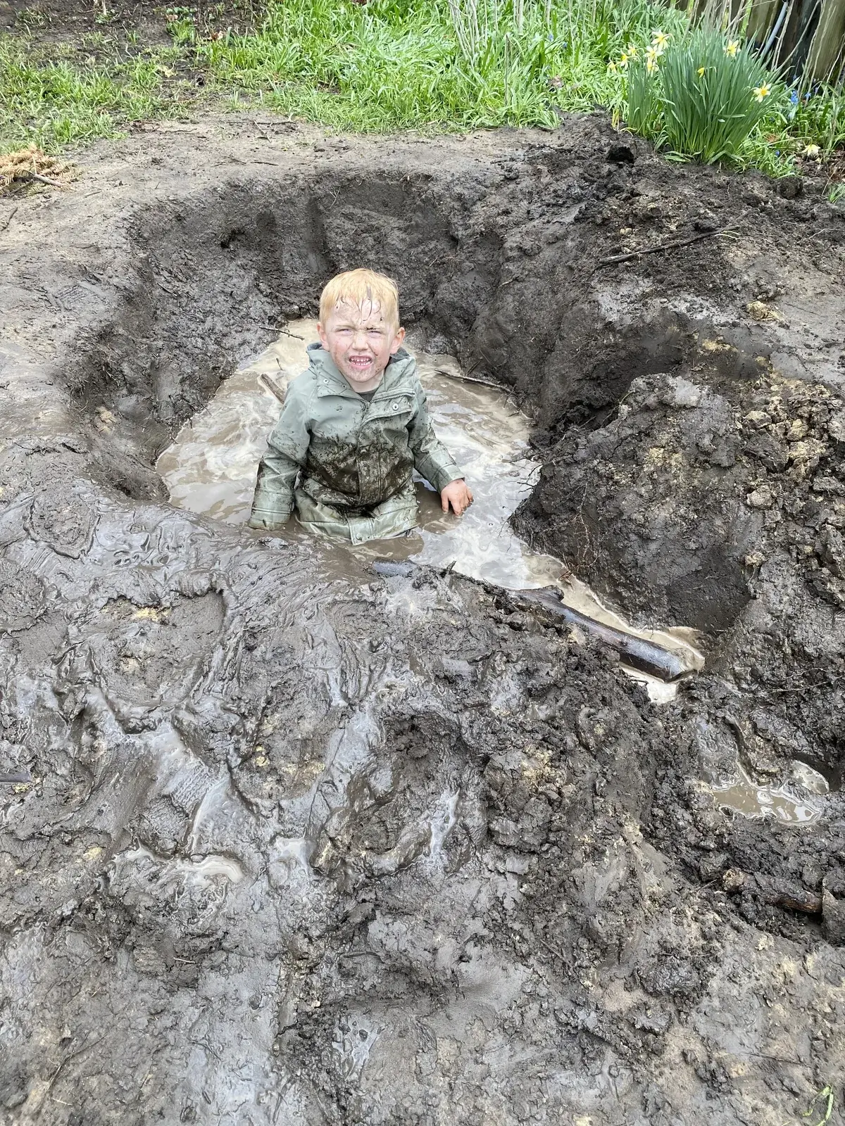 A WONDERfield student grins from inside a mud hole, covered head to toe in mud