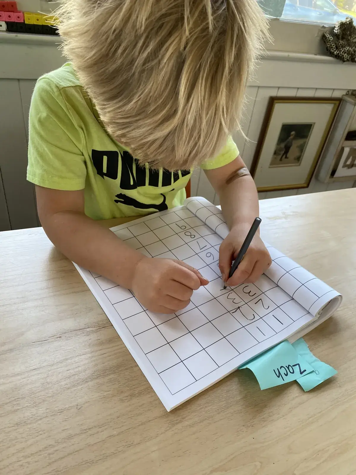 A young student practising number writing in a grid notebook