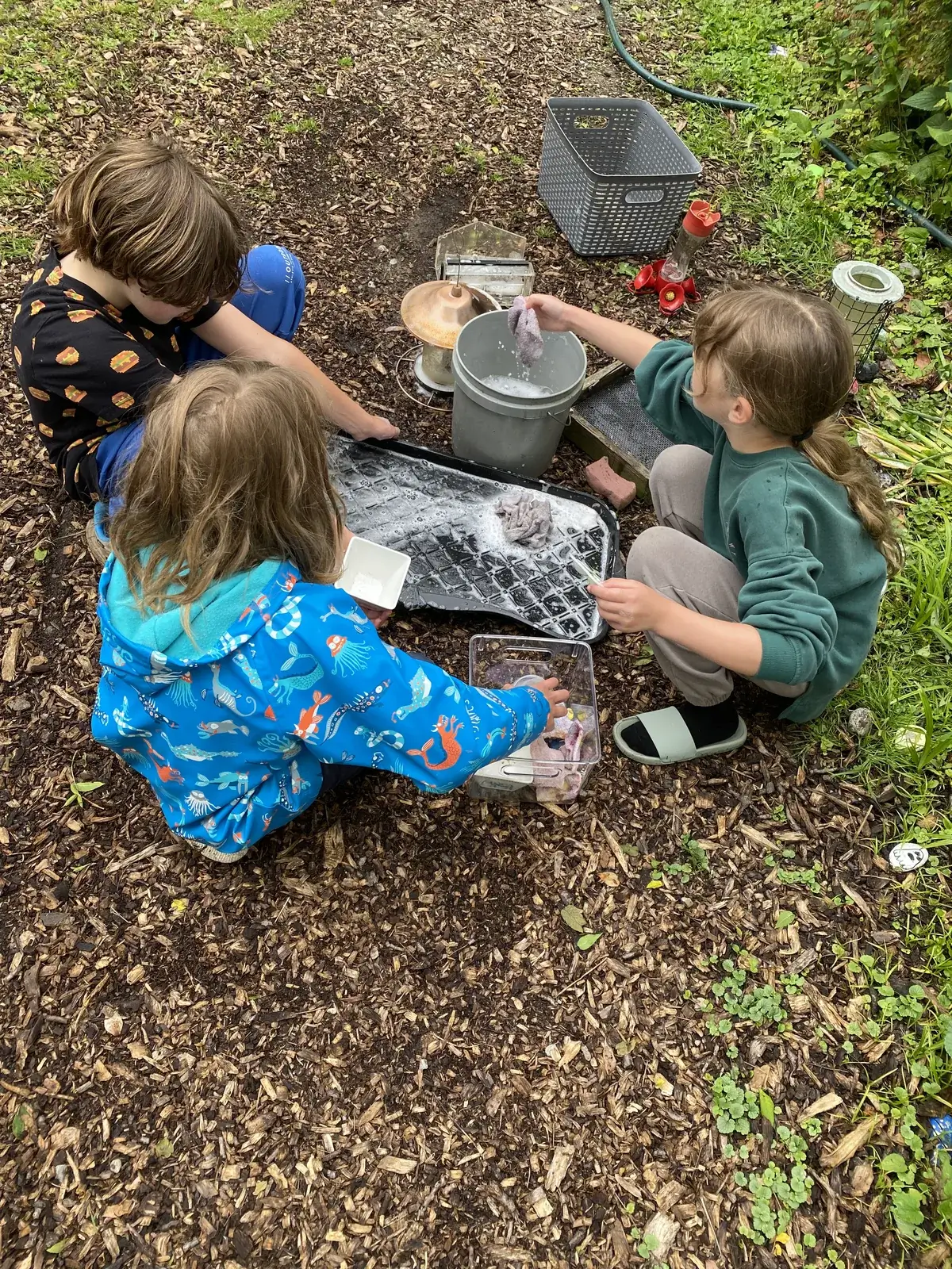 Students washing pots and pans with soap suds at the outdoor mud kitchen