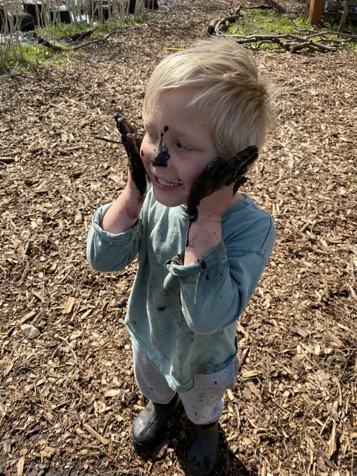 A young WONDERfield student smiles wide, hands and face covered in mud