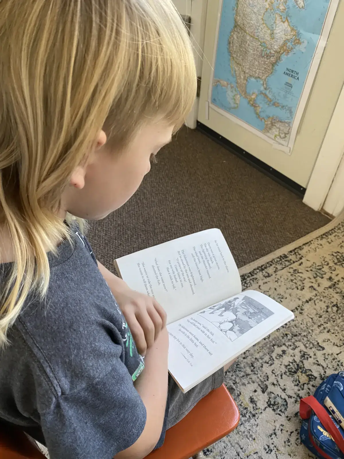 A student lying on the floor absorbed in a book, a map of North America on the wall behind
