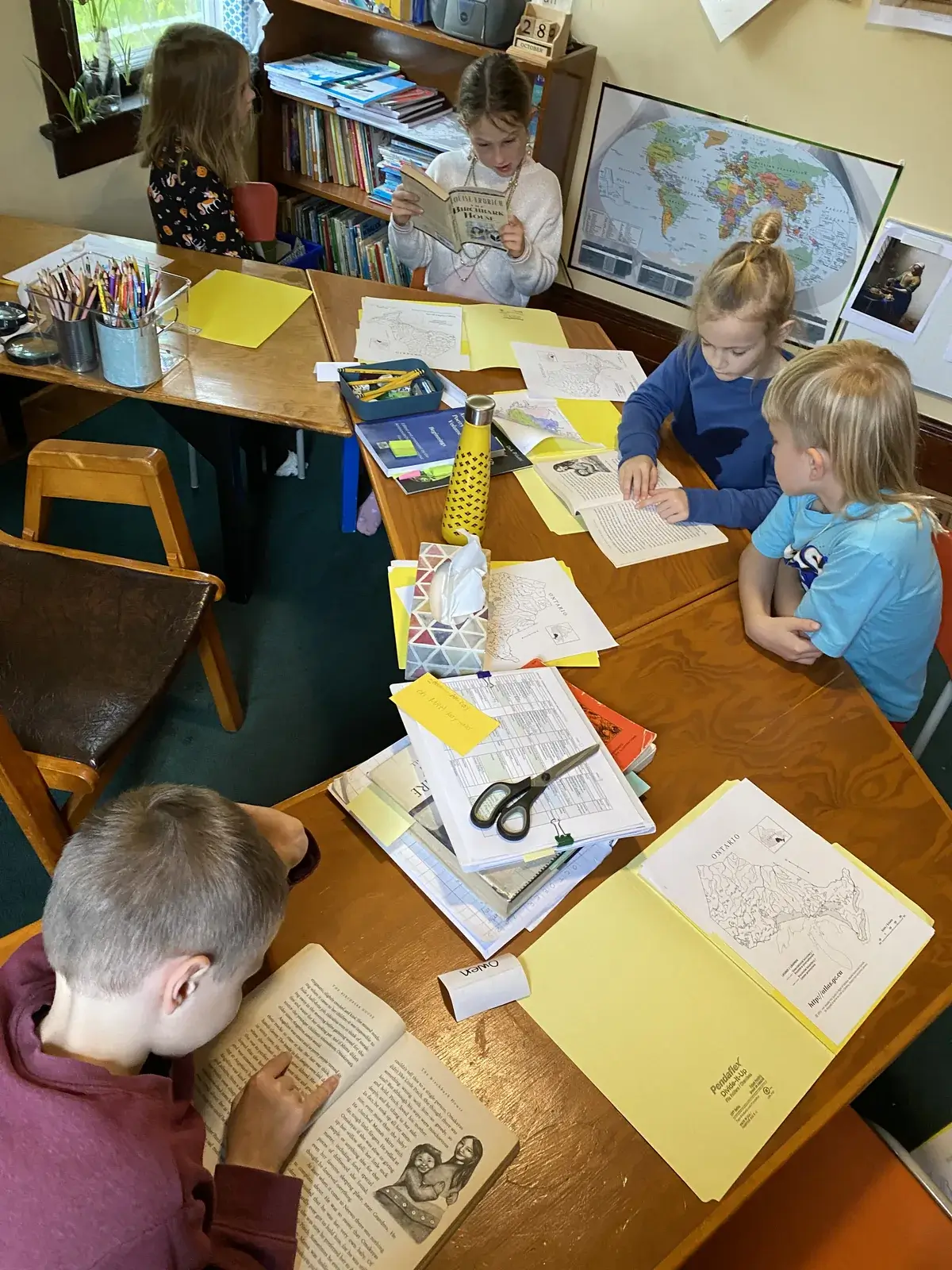 A multi-age group of students and their teacher reading together at the library table